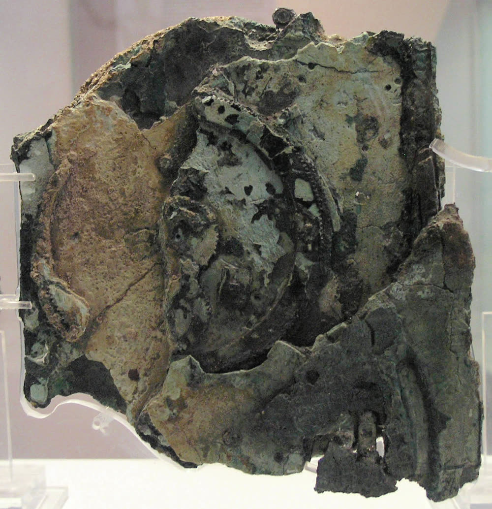 The reverse of the same fragment: a crust of green, brown and grey corrosion, with rings of fine gear teeth fused into it