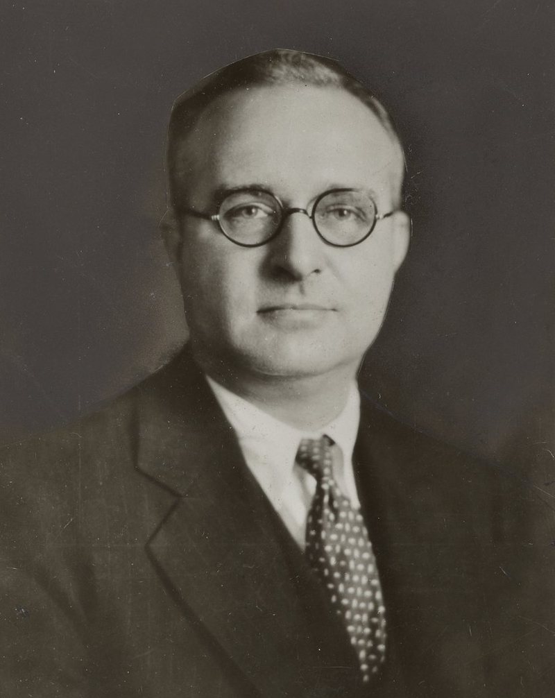 Studio portrait of Thomas Midgley Jr., a balding man in round wire glasses, a dark suit and a spotted tie.
